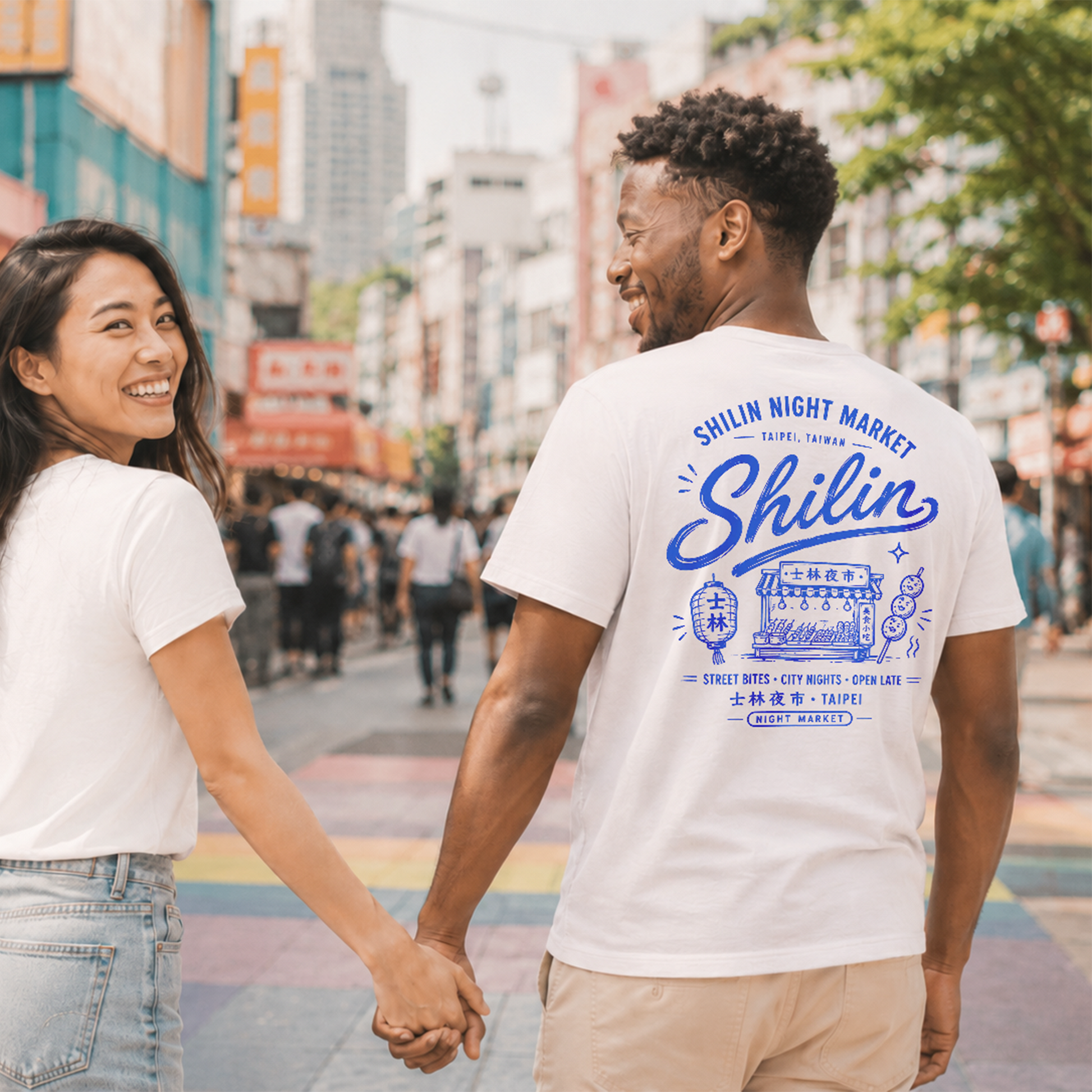 Two people holding hands on a city street, both wearing white t-shirts with 'Shilin Night Market' design.